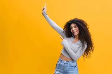 Genç şaşkın şaşkın, heyecanlı, sıradan kot gömlekli, beyaz tişörtlü, mutlu, kıvırcık kadın parmaklarını kaldırıp sarı arka plan stüdyo portresinden izole edilmiş olduğunu söylüyor. Halk yaşam tarzı konsepti
