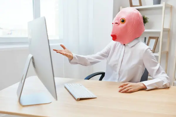 Angry businesswoman in pink fish mask screaming to desktop Raging after computer software crash error at workplace in modern office. Crazy director work online in financial corporation. Copy space