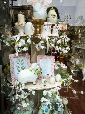 Beyaz seramik yumurta, çan ve çiçeklerle cam vitrinde sanatsal Paskalya düzenlemesi, dekor ve hediyelik eşya. Napoli, İtalya 'da Paskalyanız kutlu olsun..