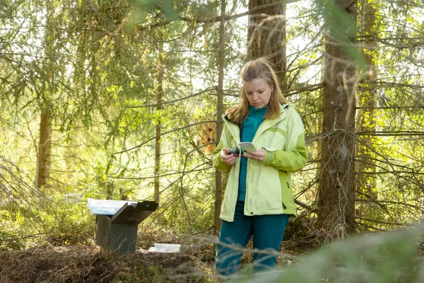 Una mujer geocaching. Las mujeres en los bosques encuentran geocache contenedor. —  Fotos de Stock