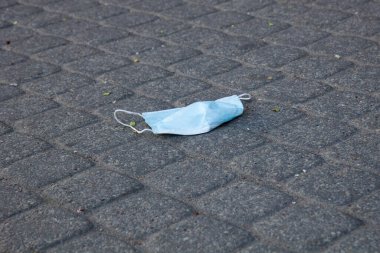 used face mask dropped on paved sidewalk