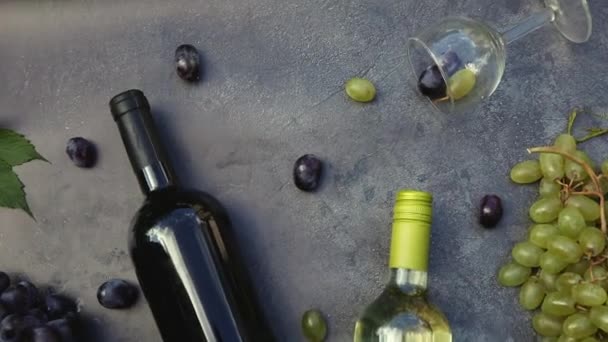Bovenaanzicht van fles rode en witte wijn, groene wijnstok, wijnglas en rijpe druif op vintage donkere stenen tafel achtergrond. Wijnwinkel wijnbar wijnmakerij of wijnproeverij concept. — Stockvideo