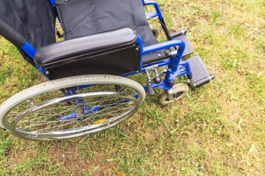 Hastane parkında çimlerde bekleyen boş tekerlekli sandalye hasta hizmetlerini bekliyor. Doğada park etmiş engelliler için geçersiz sandalye. Özürlü erişilebilir sembol. Sağlık hizmeti tıbbi konsepti