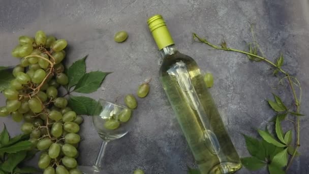 Bovenaanzicht van fles witte wijn, groene wijnstok, wijnglas en rijpe druif op vintage grijze stenen tafel achtergrond. Wijnwinkel wijnbar wijnmakerij of wijnproeverij concept. — Stockvideo