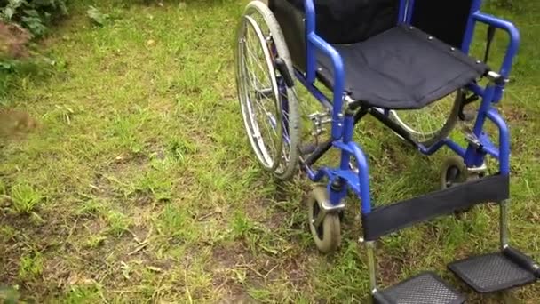 Silla de ruedas vacía de pie en el césped en el parque del hospital esperando por los servicios al paciente. Silla no válida para personas con discapacidad estacionada al aire libre en la naturaleza. Símbolo accesible para discapacitados. Concepto médico de atención médica. — Vídeos de Stock