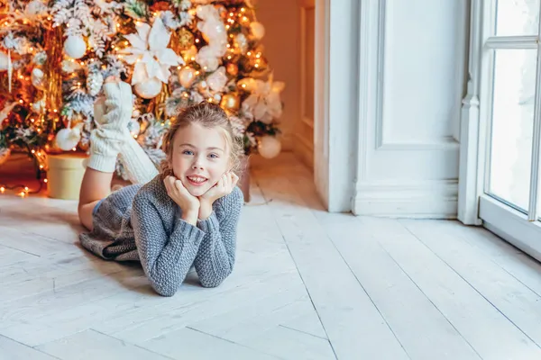 Kleines Mädchen mit Geschenkschachtel am Weihnachtsbaum zu Hause. Kleines Kind im hellen Schlafzimmer mit Winterdekoration Glückliche Familie zu Hause Weihnachten Neujahr Dezember Zeit für Feier-Konzept — Stockfoto