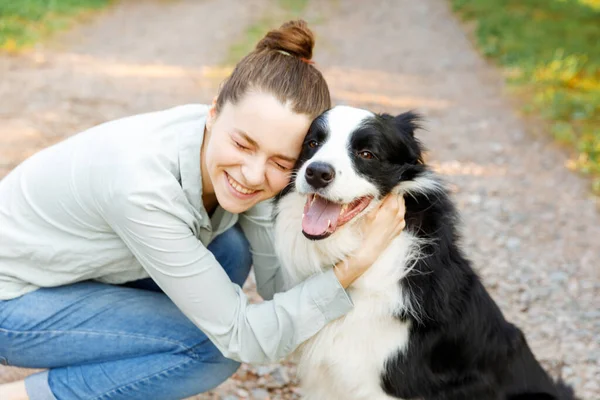 Smiling young attractive woman playing with cute puppy dog border collie on summer outdoor background. Girl holding embracing hugging dog friend. Pet care and animals concept. — Stock Photo, Image