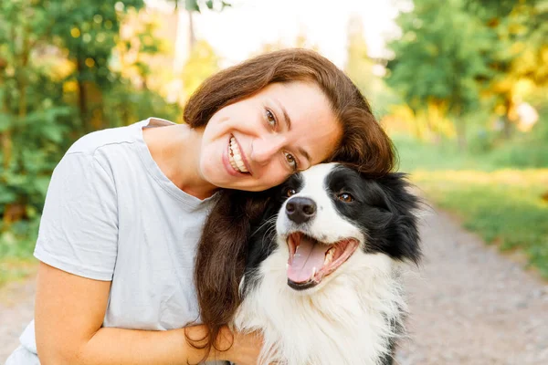 Lachende jonge aantrekkelijke vrouw spelen met schattige puppy hondengrens collie op zomer outdoor achtergrond. Meisje dat knuffelende hondenvriend omhelst. Dierenverzorging en dierenwelzijn. — Stockfoto