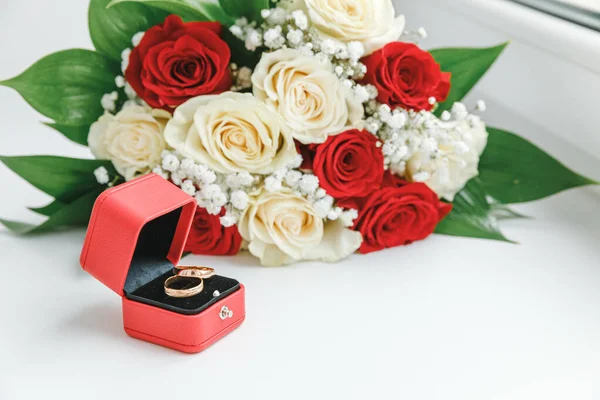 Anillos de boda de oro y ramo de flores en colores rojos blancos que yacen sobre fondo blanco. Declaración de amor, primavera. Tarjeta de boda, saludo de San Valentín. Anillos de boda. Detalles del día de boda. — Foto de Stock