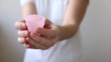 Beyaz arka planda pembe regl bardağını tutan kadın. Adet döneminde modern kadın alternatif jinekolojik hijyen. Kız elinde kan kabı.