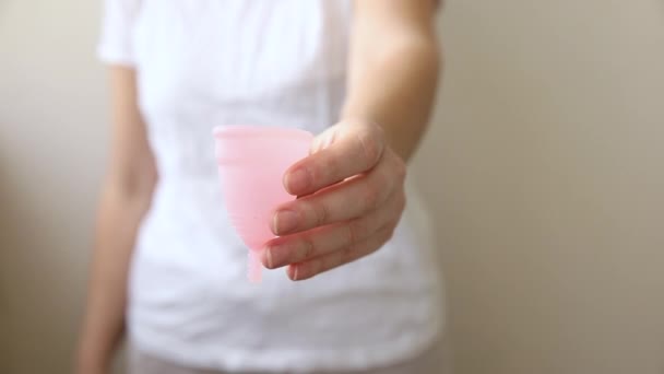 Mulher mão segurando copo menstrual rosa Isolado no fundo branco. Mulher moderna alternativa eco higiene ginecológica no período menstrual. Recipiente de sangue na mão da menina. — Vídeo de Stock