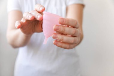 Beyaz arka planda pembe regl bardağını tutan kadın. Adet döneminde modern kadın alternatif jinekolojik hijyen. Kız elinde kan kabı.