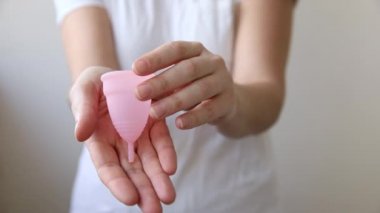 Beyaz arka planda pembe regl bardağını tutan kadın. Adet döneminde modern kadın alternatif jinekolojik hijyen. Kız elinde kan kabı.