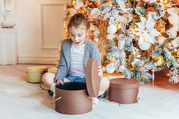 Noel arifesinde Noel ağacının yanında hediye kutusu olan küçük bir kız. Küçük çocuk kış dekorasyonlu, açık renk yatak odasında. Noel Yeni Yıl Kutlama Konsepti Zamanı.