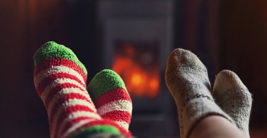Şömine arkasında yün çorapların içinde iki çift bacak. Bir çift kış ya da sonbahar akşamları evde oturup dinleniyor ve ısınıyor. Kış ve soğuk hava konsepti, Noel arifesi.
