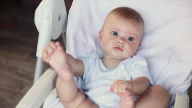 Beyaz arka planda kameraya bakan gülümseyen yeni doğmuş şirin bir kız. Bebek dinleniyor ve evdeki beslenme sandalyesine uzanıyor. Annelik mutlu çocuk konsepti.