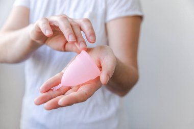 Beyaz arka planda pembe regl bardağını tutan kadın. Adet döneminde modern kadın alternatif jinekolojik hijyen. Kız elinde kan kabı.