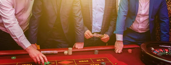 Gruppo di persone dietro tavolo da gioco roulette nel casinò di lusso. Amici che giocano a poker al tavolo della roulette con metro a nastro. Vegas giochi vita notturna fortunato concetto vincente. Bandiera . — Foto Stock
