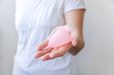 Beyaz arka planda pembe regl bardağını tutan kadın. Adet döneminde modern kadın alternatif jinekolojik hijyen. Kız elinde kan kabı.