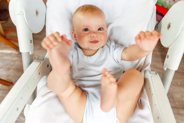 Милая маленькая новорожденная девочка с улыбающимся лицом, смотрящая на камеру на белом фоне. Младенец отдыхает, играя лежа на стуле для кормления дома. Материнство счастливый ребенок концепции. — стоковое фото