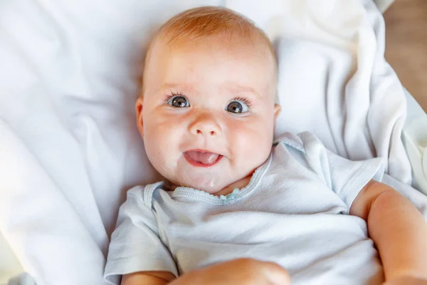 Aranyos, mosolygó arcú újszülött lány, aki fehér háttérrel nézi a kamerát. Csecsemőbaba pihen, és otthon fekszik a kiságyon. Anyaság boldog gyermek koncepció. — Stock Fotó