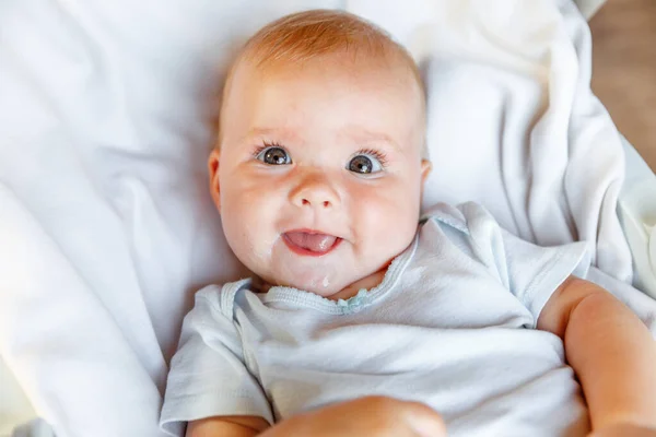 Cute little newborn girl with smiling face looking at camera on white background. Infant baby resting playing lying down on crib bed at home. Motherhood happy child concept. — Stock Photo, Image