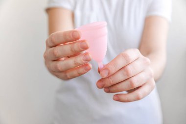 Beyaz arka planda pembe regl bardağını tutan kadın. Adet döneminde modern kadın alternatif jinekolojik hijyen. Kız elinde kan kabı.