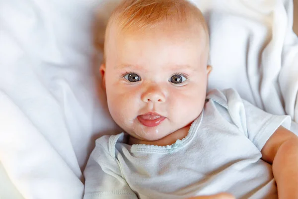 Cute little newborn girl with smiling face looking at camera on white background. Infant baby resting playing lying down on crib bed at home. Motherhood happy child concept. — Stock Photo, Image