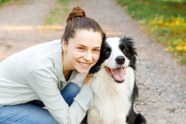 Smiling young attractive woman playing with cute puppy dog border collie on summer outdoor background. Girl holding embracing hugging dog friend. Pet care and animals concept. — Stock Photo, Image