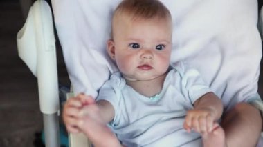 Beyaz arka planda kameraya bakan gülümseyen yeni doğmuş şirin bir kız. Bebek dinleniyor ve evdeki beslenme sandalyesine uzanıyor. Annelik mutlu çocuk konsepti.