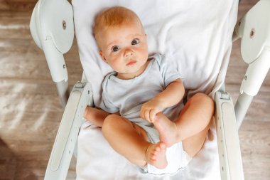 Beyaz arka planda kameraya bakan gülümseyen yeni doğmuş şirin bir kız. Bebek dinleniyor ve evdeki beslenme sandalyesine uzanıyor. Annelik mutlu çocuk konsepti.