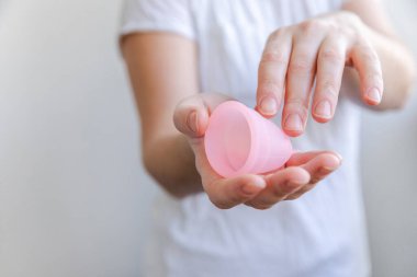 Beyaz arka planda pembe regl bardağını tutan kadın. Adet döneminde modern kadın alternatif jinekolojik hijyen. Kız elinde kan kabı.