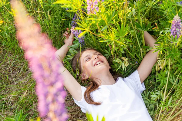 Šťastná dospívající dívka se usmívá venku. Krásná mladá dospívající žena odpočívající na letním poli s kvetoucími divokými květy zeleného pozadí. Volný šťastný dítě relaxační a užívat si přírody. — Stock fotografie