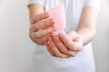 Beyaz arka planda pembe regl bardağını tutan kadın. Adet döneminde modern kadın alternatif jinekolojik hijyen. Kız elinde kan kabı.