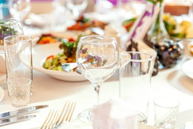 Restoranda peçete bardaklarıyla yemek masası, lüks bir iç mekan. Şık bir düğün ziyafeti dekorasyonu ve yemek servisi tarafından beyaz masa örtüsü üzerinde hazırlanmış yiyecekler..