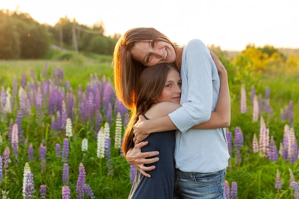 Jeune mère embrassant son enfant en plein air. Femme et adolescente sur le champ d'été avec des fleurs sauvages floraison fond vert. Bonne famille maman et fille jouer sur prairie. — Photo