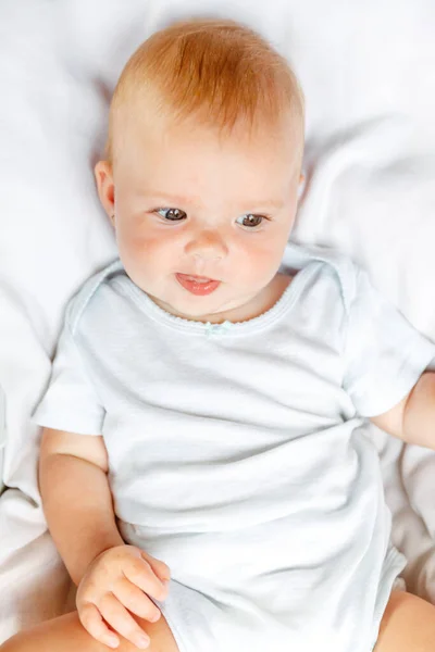 Cute little newborn girl with smiling face looking at camera on white background. Infant baby resting playing lying down on crib bed at home. Motherhood happy child concept. — Stock Photo, Image