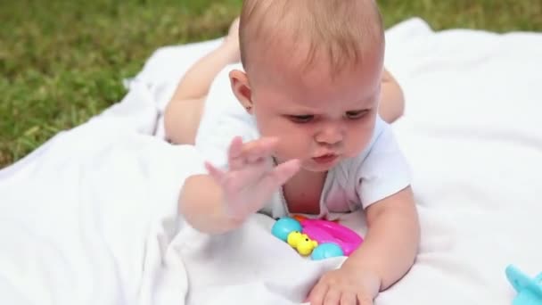 En liten nyfödd flicka som ligger på magen och tuggar på filt, sommardag utomhus. Spädbarn som har kul utomhus. Barnet vilar och leker och lär sig krypa. Barndomskoncept för moderskap — Stockvideo