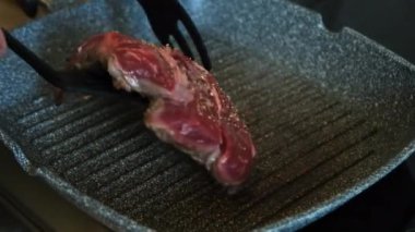Şef, profesyonel mutfakta ızgara tavada etli biftek pişiriyor. Erkek eli ızgarada biftek kızartır. Lezzetli, modern mutfak.
