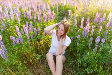 Dışarıda gülümseyen genç bir kadın. Güzel esmer kız kır çiçeklerinin açtığı yeşil arka planla yaz tarlasında dinleniyor. Yazın özgür ve mutlu bir kadın. Özgürlük mutluluğu tasasız mutlu insanlar konsepti