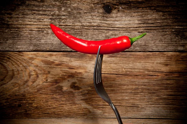 En red hot chilipeppar på en gaffel över gamla träbord — Stockfoto