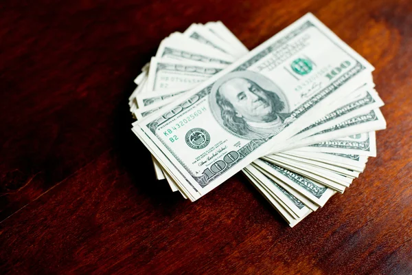 Stosy banknotów stu dolarów na drewniane biurko — Zdjęcie stockowe