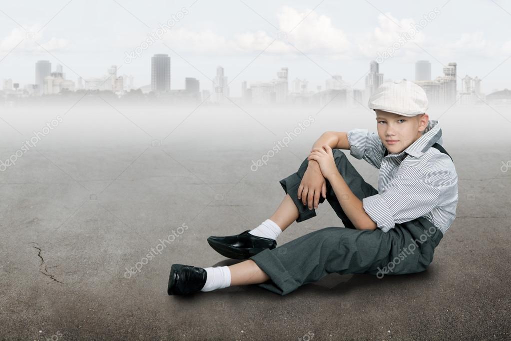 Old fashioned boy sitting on a ground near city