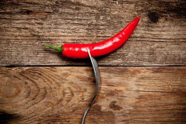 Eine rote Chilischote auf einer Gabel über einem alten Holztisch — Stockfoto