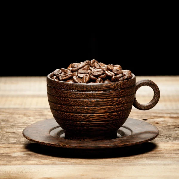 Wooden cup with coffee-beans on wooden table — Stock Photo, Image