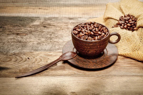 Tazza di legno con chicchi di caffè sul tavolo di legno — Foto Stock