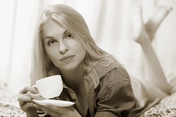 Kvinna liggande på sängen och dricker kaffe och leende. — Stockfoto