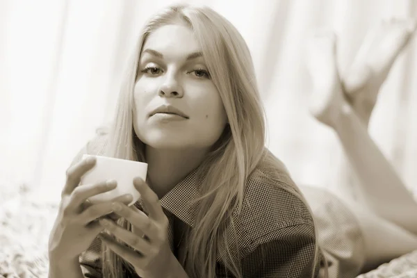 Frau am Bett liegend, Kaffee trinkend und lächelnd. — Stockfoto