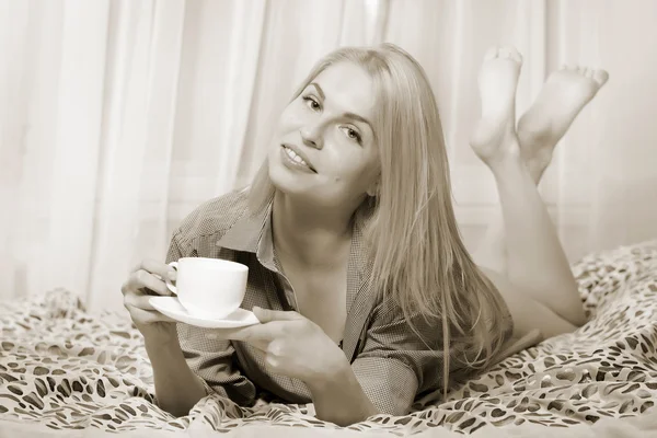 Mujer acostada en la cama y tomando café y sonriendo . —  Fotos de Stock