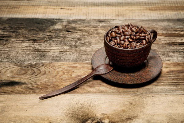 Copo de madeira com grãos de café na mesa de madeira — Fotografia de Stock